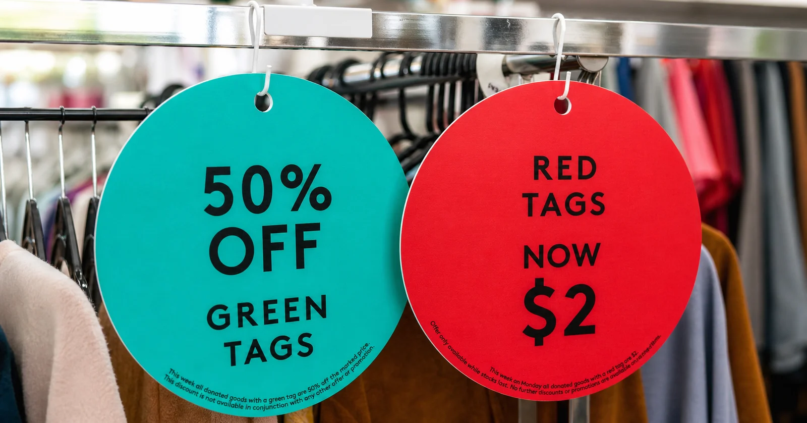 Two Salvos sale tags hanging from a clothing rack: one green tag for 50% off and one red tag for $2 items.